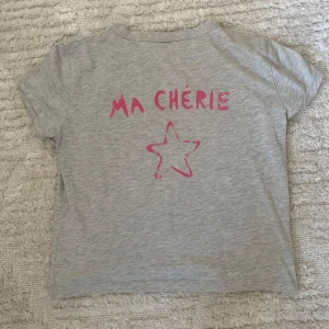 Grå t-shirt med rosa tryck 'Ma Chérie' - Gina T-shirt med Ma Cherie tryck. Säljer då den är för liten på mig. Ser nästan ny ut och har använts ett fåtal ggr. Storlek 158/164 men är som en babytee så lite mindre i storleken. Kontakta gärna om det finns några funderingar. 