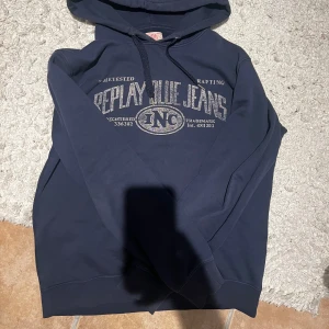 Mörkblå hoodie från Replay - Säljer en snygg mörkblå hoodie från Replay Blue Jeans med tryck framtill. Den har en klassisk huva med dragsko och är perfekt för en avslappnad stil. Passar bra till jeans eller joggers. Vintage rare replay hoodie i över bra skick. 