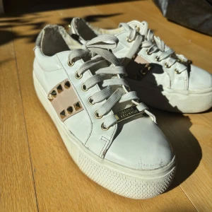 Vita sneakers med nitar från Steve Madden - Snygga vita sneakers från Steve Madden med coola nitar på sidorna och en platåsula. Skorna har snörning och en metallic-detalj vid hälen som ger en extra touch. Dom är lite slitna på insidan men inget som syns på. Diskutera gärna priset och skickar fler bilder 🥰