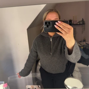 Mörkgrå stickad tröja med dragkedja  - Mysig mörkgrå stickad tröja från H&M med halv dragkedja framtill. Tröjan har långa ärmar och en avslappnad passform, perfekt för kyliga dagar. Snygg och enkel att matcha med det mesta.