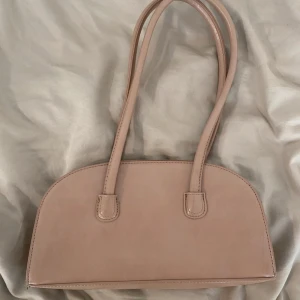 Beige axelväska - Säljer en stilren beige axelväska med rundad form och långa handtag. Väskan har ett huvudfack med dragkedja och magnetknäppning. Superfin!🩷🩷🩷🩷