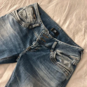 Blåa jeans från LTB - Snygga blå low waist jeans från LTB med klassisk femficksdesign och ljusa slitningar. Byxorna har normal passform och raka ben. Använd fåtals gånger