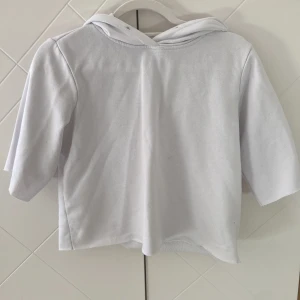 Vit hoodie med trekvartsärm - Säljer en stilren vit hoodie med trekvartsärm. Perfekt för en avslappnad look. Den har en klassisk huva och är gjord i ett mjukt material.