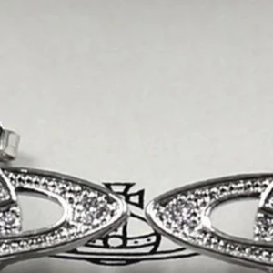 Silverfärgade örhängen med strass från Vivienne Westwood - Säljer ett par ikoniska örhängen i silverfärg från Vivienne Westwood. De har planetformad design med gnistrande strass och klassisk orb-detalj. Perfekta för att ge din look en cool och trendig touch.