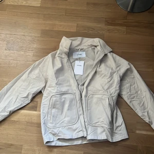 Beige jacka från Whyred - Säljer en stilren beige jacka från Whyred. Jackan har en dragkedja framtill och två stora fickor. Perfekt för vår och höst med sin klassiska design och bekväma passform. Storlek M, helt ny! Skriv för funderingar! Ny pris 2299kr