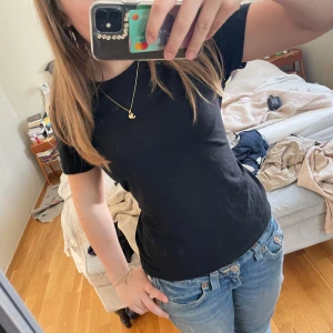 Topp med knytning i ryggen - Säljer en stilren svart t-shirt med korta ärmar och knyt i ryggen. Perfekt för en avslappnad look. Passar till jeans eller kjol. Liten defekt vid knytet på baksidan ❣️❣️Själva T-shirten är från Lager 157, men är köpt från ett UF-företag!