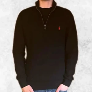 Svart half zip från Ralph Lauren - Snygg svart half zip från Polo Ralph Lauren med den ikoniska röda loggan på bröstet. Perfekt för en stilren look. Den är i fint skick och i storlek M. Vid några frågor eller funderingar är det bara att höra av sig.