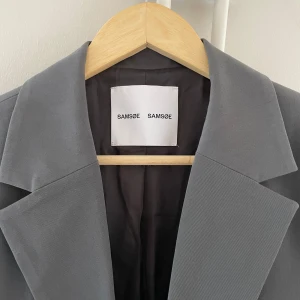 Grå kavaj från Samsøe Samsøe (diskuterbart pris!!) - Snygg grå kavaj från Samsøe Samsøe med klassisk design och två knappar framtill. Perfekt för en stilren look. Kavajen har långa ärmar och är tillverkad i ett elegant material. Priset är diskuterbart så kom med prisförslag!💞