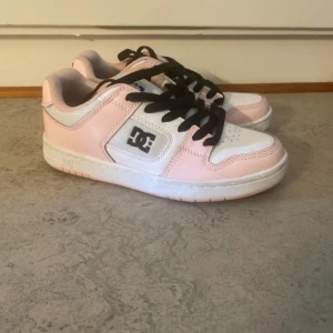 Rosa och vita sneakers från DC - Säljer ett par snygga sneakers från DC i rosa och vitt. Skorna har svarta snören och DC-loggan på sidan och hälen. Perfekta för en avslappnad stil.