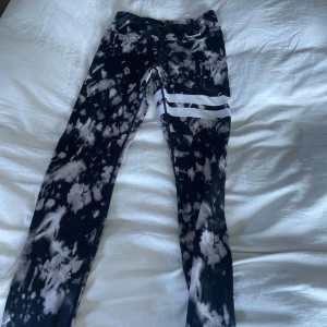 Svarta och vita leggings med mönster - Snygga svarta och vita leggings från Stronger med ett coolt batikmönster. De har en elastisk midja och två vita ränder på ena benet. Perfekta för träning eller en avslappnad dag.
