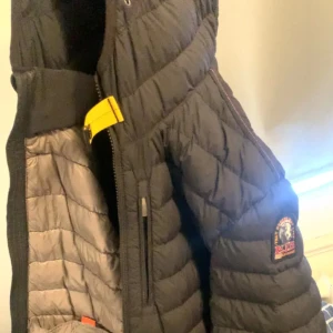 Svart quiltad jacka från Parajumpers - Säljer en svart quiltad jacka från Parajumpers med en snygg gul detalj vid kragen. Jackan har en dragkedja och är perfekt för kyligare dagar. Insidan är grå och ger en fin kontrast. Passar både till vardag och äventyr.