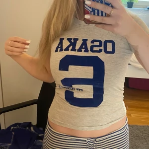 Grå t-shirt med blå tryck - Säljer en grå croppad t-shirt med blå text och siffra på framsidan. 