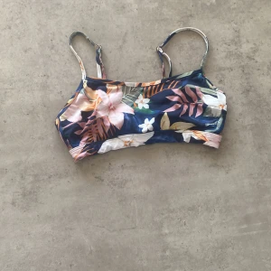 Blommig bikiniöverdel - Snygg bikiniöverdel med blommigt mönster i blått, rosa och grönt. Justerbara axelband för perfekt passform. Perfekt för en dag på stranden eller vid poolen!