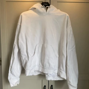 Vit hoodie från Weekday - Säljer en stilren vit hoodie från Weekday i storlek M. Den har en klassisk design med en stor ficka framtill och en bekväm huva med dragsko. Perfekt för en avslappnad look.