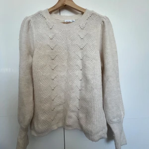 Beige stickad tröja från VILA - Mysig beige stickad tröja från VILA med diskret mönsterstickning framtill. Tröjan har rund halsringning och långa ärmar med ribbade muddar. Perfekt för lager-på-lager under kyliga dagar. Tröjan är storlek L men passar även mig som i vanliga fall bär XS.