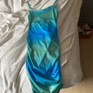 Blågrön omlottklänning med smala axelband från SHEIN - Säljer en snygg blågrön klänning från SHEIN med smala axelband och öppen rygg med snörningsdetaljer. Klänningen har en tight passform och är tillverkad i ett mjukt, syntetiskt material. Perfekt för sommarens alla tillfällen!