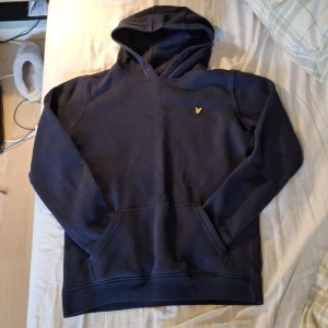 Mörkblå hoodie från Lyle & Scott Junior - Säljer en mörkblå hoodie från Lyle & Scott Junior med klassisk gul logga på bröstet. Tröjan är en skön tröja som är väldigt behaglig som också är rätt så varm. Som är bra till kalla dagar och svala kvällar. 