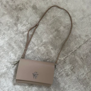 Beige axelväska från CW - Superfin beige väska från Carin Wester. Endast använd i 4 dagar på en semester så helt i nyskick förutom att själva märket fått lite repor. Bra med olika fack inuti samt går att stänga med både knapp och dragkedja.