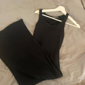 Svart ribbad långklänning  - Säljer en svart ribbad långklänning. Klänningen är ärmlös med rund halsringning och har en tight passform. Perfekt för dig som gillar en enkel och stilren look.