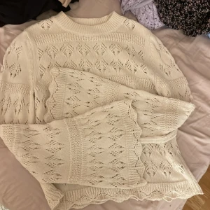 Vit stickad tröja med spetsdetaljer - Säljer en vacker vit stickad tröja med spetsdetaljer och ett fint mönster. Tröjan har långa ärmar och en ribbad krage. Perfekt för kyliga dagar och ger en romantisk touch till din outfit.