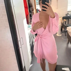 Ljusrosa omlottklänning med knytband - Säljer en söt ljusrosa omlottklänning med knytband i midjan och långa ärmar. Klänningen har v-ringning och är perfekt för vår och sommar. Enkel och stilren design som passar till många tillfällen.