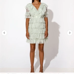 By Malina klänning - Superfin ljusgrön klänning med flera lager volanger och spetsdetaljer. Djup v-ringning och kort ärm, perfekt för speciella tillfällen. Klänningen har en feminin siluett och kort längd.