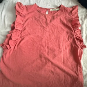 Rosa blus med volangdetaljer - Supersöt rosa blus från Carin wester med volanger längs axlarna och ärmlös design. Aldrig använd Storlek 42/L/XL skriv gärna om du vill se mer bilder! 🩷