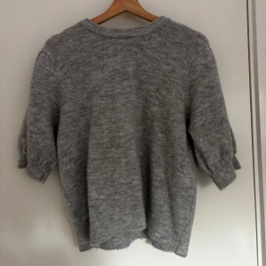 Grå stickad tröja - Mysig grå stickad tröja med rund halsringning och långa ärmar. Tröjan har en avslappnad passform och ribbade muddar vid ärmslut och nederkant. Perfekt för kyliga dagar.