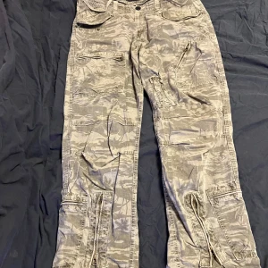 Grå camo cargobyxor från Fishbone - Säljer ett par grå cargobyxor från Fishbone med ett coolt camouflagemönster. Byxorna har flera praktiska fickor och en knappstängning i midjan. Lite slitet på vänstra baksidan vid benet men går att sy🫶🏻