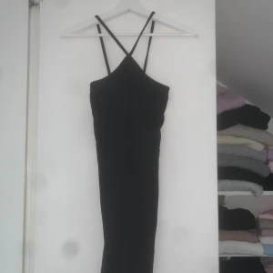 Svart klänning - Svart klänning från Noisy May med smala axelband som korsas i bröstet. Klänningen har en tight passform och är ärmlös med stilren, minimalistisk design. Perfekt för dig som gillar en enkel men snygg look.