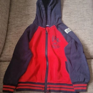 Röd och mörkblå hoodie  - Säljer en snygg hoodie från Lupilui i rött och mörkblått. Tröjan har huva, dragkedja framtill och ribbade muddar med ränder. Tryck på bröstet med texten 'Grr not angry trouble tiger'. Utöver att färgen är något blekt vid Utöver att färgen är något blekt vid muddarna (se bild) så hittar jag inga skavanker. Stl 98/104 #kassfantasi98104 #kassfantasi98 #kassfantasi104