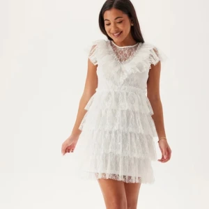 Fin studentklänning  - Superfin vit kort klänning i spets med flera lager volanger och v-ringning. Klänningen har pärlknappar i ryggen, transparenta spetsdetaljer upptill och korta ärmar. Använd endast 1 gång. Nypris 999kr. Perfekt för dig som tar studenten 2026!