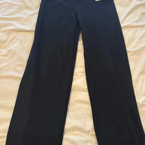 Svarta kostymbyxor från Nelly, L - Snygga svarta kostymbyxor från Nelly i modellen Keep it Up Low Waist Suit Pants. Byxorna har låg midja och raka, vida ben för en trendig look. Perfekta att styla med crop top eller oversized skjorta. Helt nya ligger fortfarande i sin plats och lappen kvar 