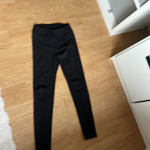 Svarta leggings från Iconic - Svarta leggings från Iconic med hög midja och tight passform. Tillverkade i ett stretchigt syntetmaterial som sitter skönt och följsamt. Perfekta för träning eller när du vill ha en enkel och stilren look.
