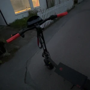 KuKirin G4 Pro El-scooter - KuKirin G4 Pro el-scooter med digital display, nyckelstart och röda handtag. Scootern ser ut att vara i gott skick med minimalt synligt slitage. Perfekt för pendling med stark motor och lång räckvidd. Laddare och nyckel medföljer.