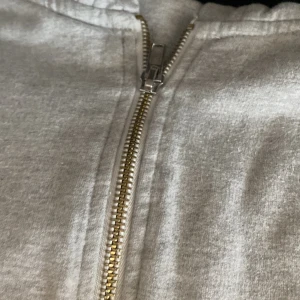 Grå Moncler hoodie med dragkedja - Snygg grå hoodie från Moncler med hel dragkedja framtill, broderade Moncler-loggor på bröstet och ärmen samt huva med breda snören. Tillverkad i mjuk bomull för en skön och avslappnad stil.