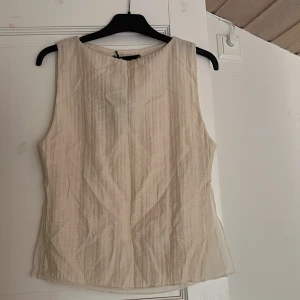 Beige topp  - Säljer en stilren beige topp från Bik Bok i storlek S. Toppen är ärmlös med rund halsringning och har en lätt skimrande, strukturerad yta. Materialet känns luftigt och toppen har en rak, enkel passform som är perfekt för fina tillfällen! Även vardags med. Helt ny med prislapp, 299kr nypris  tyvärr lite sminkfläck ifrån när jag köpte den… går bort i tvätten!