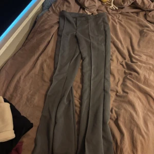 Grå kostymbyxor med bootcut - Snygga grå kostymbyxor med bootcut-snitt och pressveck längs benen. Byxorna har klassisk midja och stängs med knapp och dragkedja. Perfekta för en stilren och trendig look.