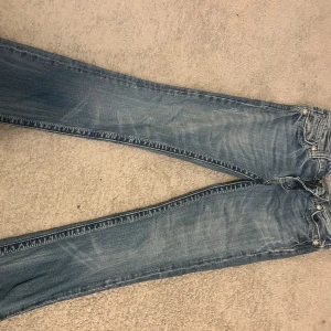 Blå jeans med broderade bakfickor - Snygga blå jeans med slitningar och coola broderade detaljer på bakfickorna. Klassisk femficksmodell med raka ben och silverfärgade nitar. Perfekta för dig som vill sticka ut lite extra med detaljer på jeansen. Pris kan diskuteras (jag betalar frakten)