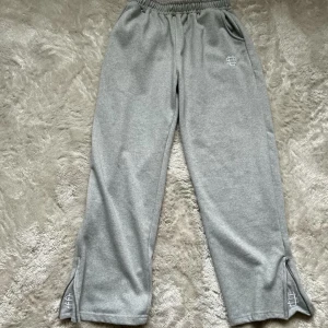 Grå mjukisbyxor från Suvene - Snygga grå mjukisbyxor från Suvene med elastisk midja och broderad vit logga på höften och vid bensluten. Byxorna har raka ben med slitsar nertill och är tillverkade i mjukt bomullsmaterial. Även en flared stil! Perfekta för en chill och avslappnad stil! 