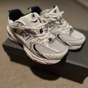 Vita New Balance sneakers mesh & skinn - Snygga vita New Balance sneakers med mesh och skinnpaneler, detaljer i silver och svart. Klassisk chunky sula och snörning framtill. Perfekta för dig som gillar sportig och trendig stil.