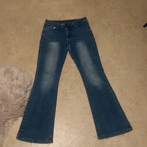 Blå bootcut jeans med detaljer - Snygga blå bootcut jeans med slitningar och ljus tvätt. Bakfickorna har coola broderade mönster och nitar, samt lock med knapp. Klassisk femficksmodell och normal passform. Perfekta för dig som gillar jeans med lite extra detaljer. Priset kan diskuteras 