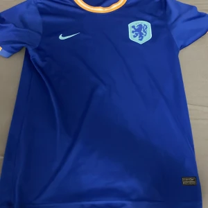 Blå Nederländerna Nike fotbollströja - Säljer en blå Nederländerna fotbollströja. Tröjan har korta ärmar, broderad landslagssköld och Nike-logga på bröstet. perfekt för match eller träning.