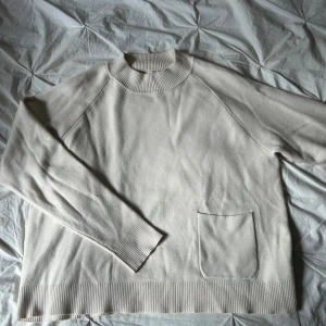 Vit stickad tröja Carin Wester  - Vit/creme vit stickad tröja från Carin Wester i storlek M. Tröjan har en bred ribbad krage, långa ärmar och en enkel ficka framtill. Ribbade muddar vid ärmslut och nederkant ger en clean look.