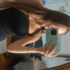 Svart one shoulder topp - Säljer en svart one shoulder topp med lätt skrynklig struktur. Toppen är figurnära och har en axelbandslös sida samt bredare axelband på andra sidan. Perfekt för dig som gillar en stilren och trendig look.