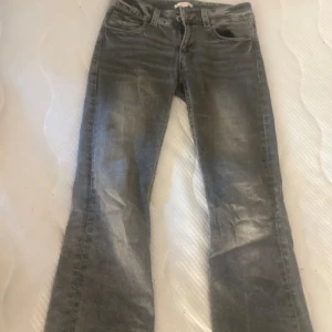 Grå bootcut jeans från Gina Tricot - Snygga grå jeans från Gina Tricot i lowwaist bootcut-modell. Jeansen har coola detaljer på bakfickorna med broderade mönster och knappar. Klassisk femficksdesign, bälteshällor och dragkedja framtill.  
