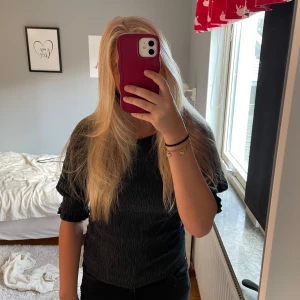 Svart ribbad topp från Lindex XS - Säljer en svart ribbad topp från Lindex i storlek XS. Toppen har korta puffärmar med volangdetalj vid ärmslut och en smickrande, figurnära passform. Materialet är stretchigt och strukturerat vilket ger en cool look.