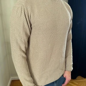 Beige stickad tröja med struktur - Säljer en beige stickad tröja med snygg struktur och rund hals. Tröjan har långärmade ärmar och en klassisk, avslappnad passform. Perfekt för lager-på-lager och enkel att matcha med jeans eller andra byxor.