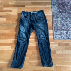Stanwick blå jeans med tryck - Snygga blå jeans från Stanwick med coolt vitt tryck på bakfickan och insidan av linningen. Jeansen har raka ben, klassiska fickor och markerade sömmar över knäna för en extra streetkänsla. Perfekta för dig som gillar en avslappnad men trendig look.