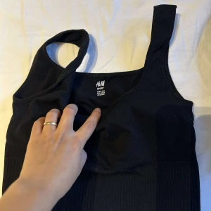 Svart sportig linnetopp från H&M - Säljer en svart sportig linnetopp från H&M med breda axelband och ribbad nederkant. Toppen är ärmlös och har en tight passform, perfekt för träning eller chill dagar. Enkel och stilren design som är lätt att matcha med andra plagg.